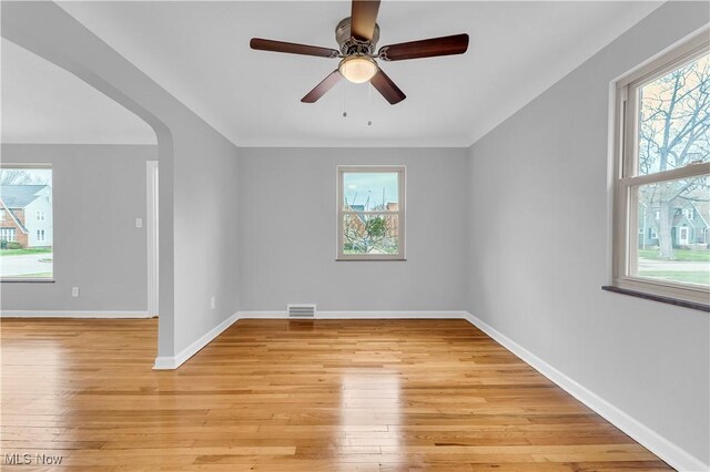 empty room with light wood-style floors, baseboards, ceiling fan, and arched walkways