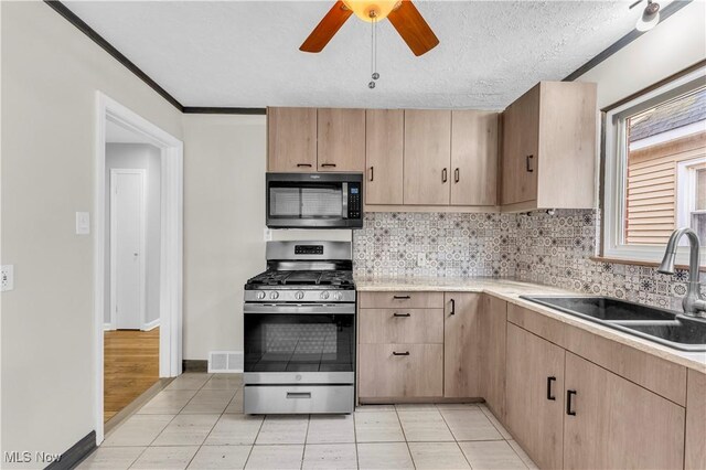 kitchen featuring stainless steel range with gas cooktop, light brown cabinets, a sink, decorative backsplash, and a textured ceiling