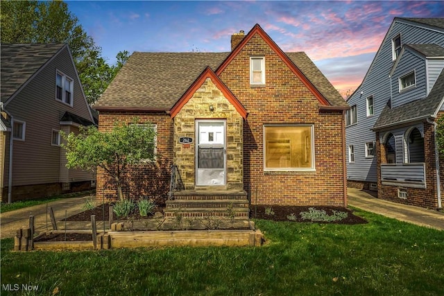 english style home featuring a chimney, brick siding, entry steps, and a yard