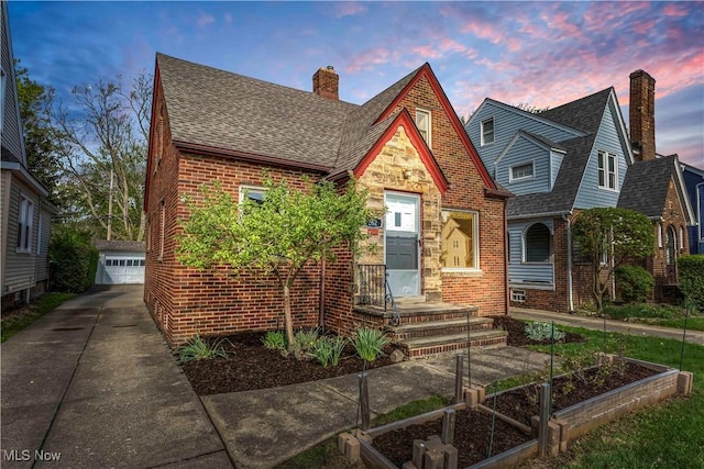 tudor home featuring brick siding, a chimney, a shingled roof, an outdoor structure, and a detached garage