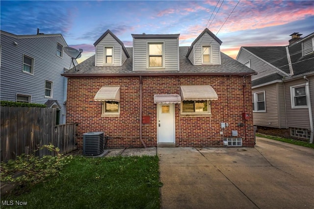 view of front of home with brick siding, fence, a patio area, central air condition unit, and roof with shingles