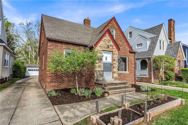 tudor house featuring brick siding, a shingled roof, a chimney, a detached garage, and an outdoor structure