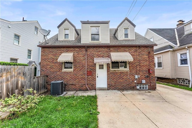 rear view of house with brick siding, fence, a patio area, cooling unit, and roof with shingles