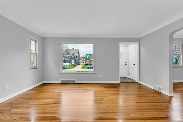 unfurnished living room with arched walkways, light wood finished floors, and baseboards