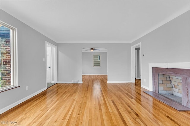 unfurnished living room featuring light wood-type flooring, a fireplace with raised hearth, a ceiling fan, and baseboards