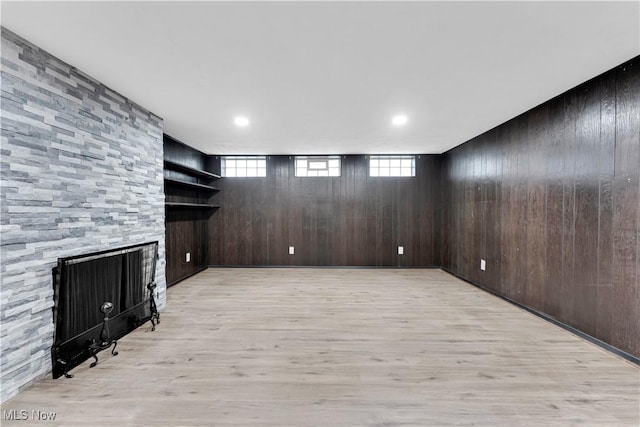 below grade area featuring light wood finished floors, wooden walls, and a fireplace