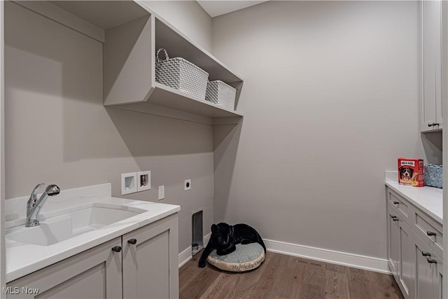 washroom featuring electric dryer hookup, washer hookup, wood finished floors, baseboards, and cabinet space