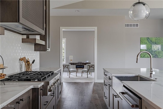 kitchen featuring dark wood-style flooring, dark brown cabinetry, backsplash, stainless steel appliances, and light stone counters