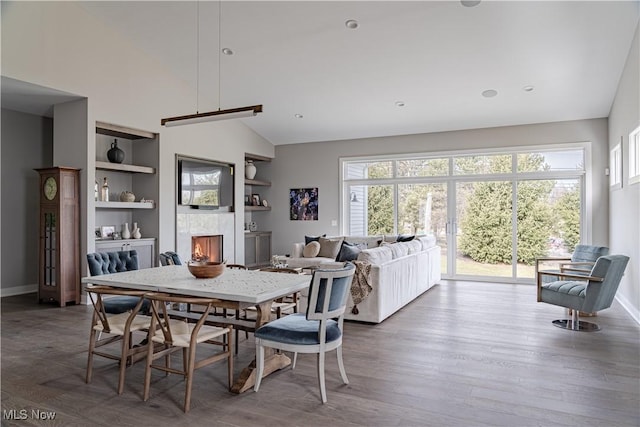 dining room featuring built in shelves, baseboards, wood finished floors, plenty of natural light, and high vaulted ceiling