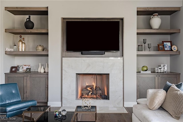 living room with built in features, a fireplace, baseboards, and wood finished floors