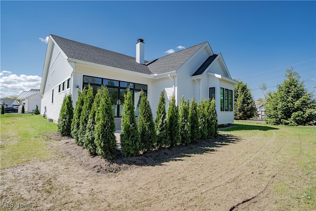 rear view of house with a chimney, a yard, and a shingled roof
