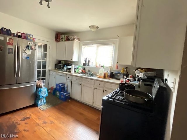 kitchen with appliances with stainless steel finishes, white cabinetry, light wood finished floors, light countertops, and a sink