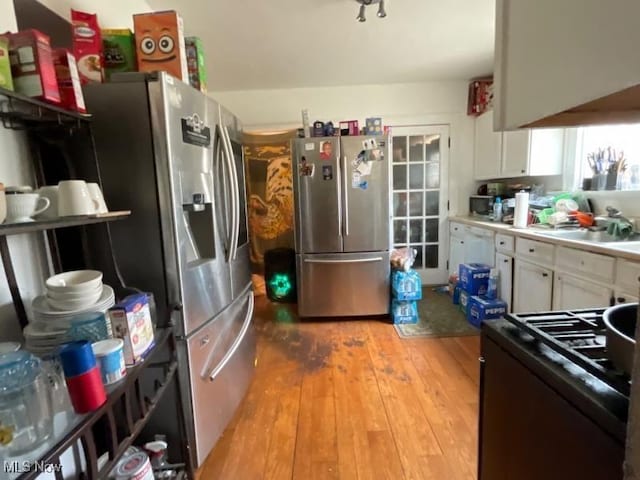 kitchen with freestanding refrigerator, black gas stove, light wood-style floors, white cabinets, and light countertops