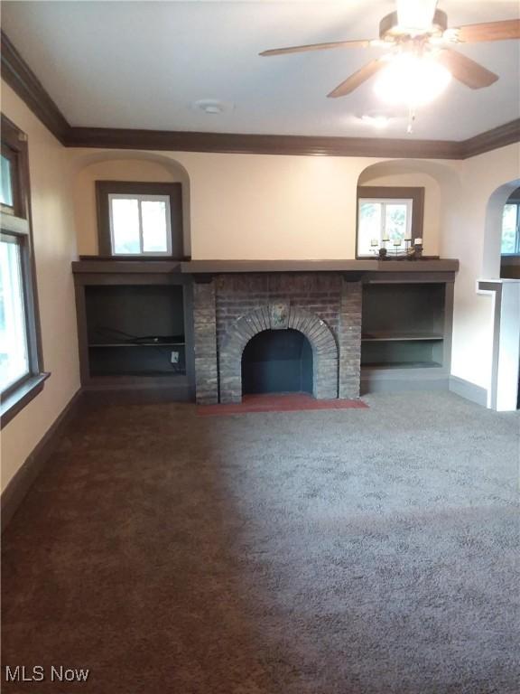 unfurnished living room featuring ornamental molding, a brick fireplace, carpet, baseboards, and a ceiling fan