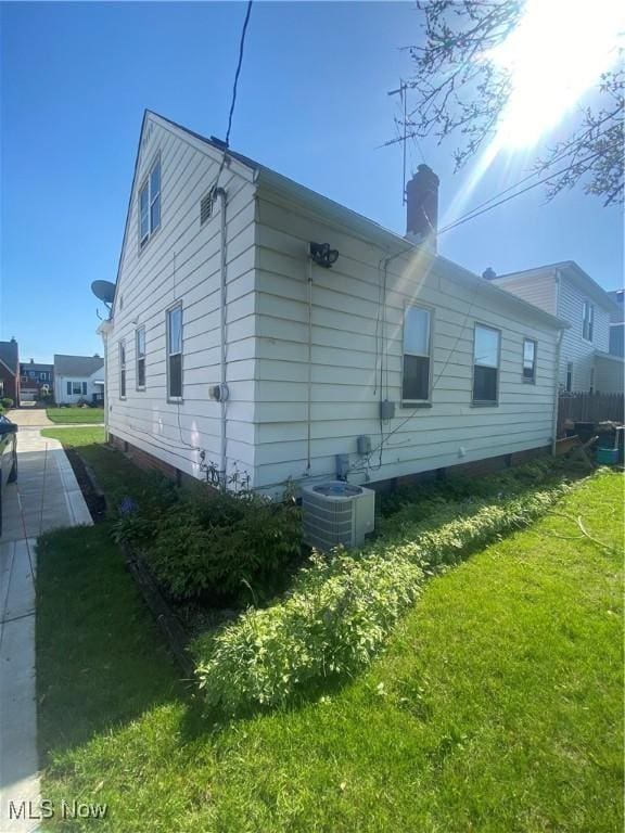 view of side of property featuring central AC, a chimney, and a yard