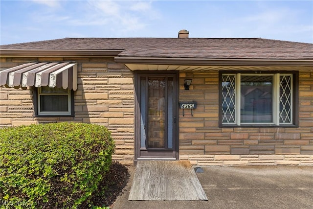 doorway to property featuring a shingled roof and stone siding