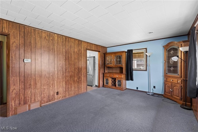 unfurnished living room featuring wooden walls, carpet floors, and baseboards