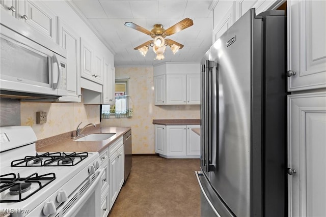 kitchen with appliances with stainless steel finishes, a sink, a ceiling fan, white cabinets, and wallpapered walls