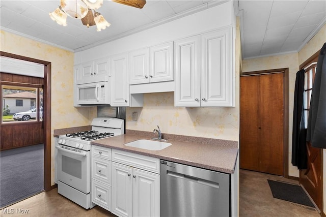 kitchen with white appliances, a sink, wallpapered walls, white cabinets, and ornamental molding