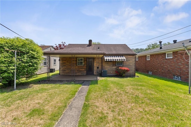 back of property with central air condition unit, a lawn, stone siding, a chimney, and a patio area