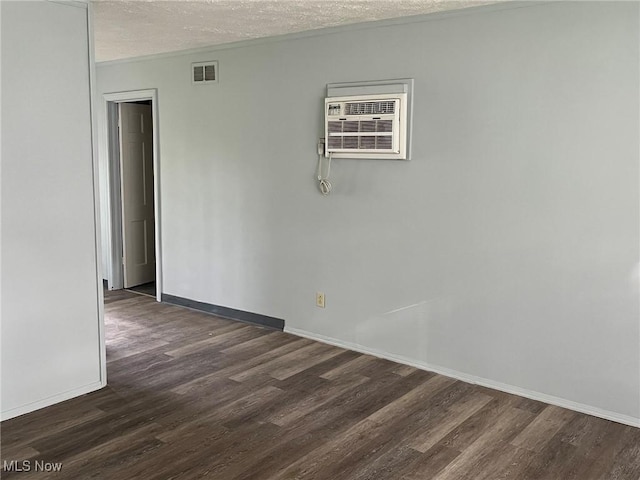 empty room with dark wood-style flooring, baseboards, a textured ceiling, and a wall mounted air conditioner
