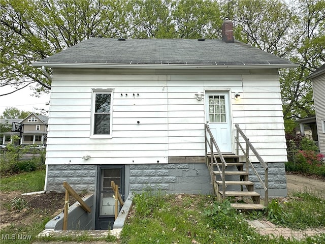 rear view of property with entry steps, a chimney, and roof with shingles