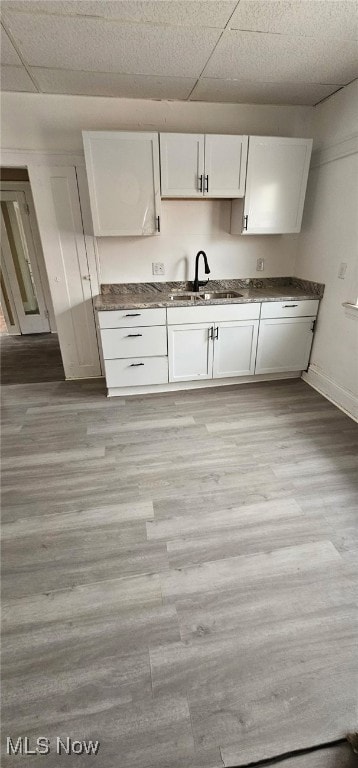 kitchen featuring dark countertops, a sink, light wood-style floors, and white cabinets