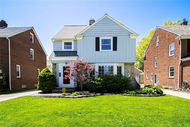 view of front of home with board and batten siding, a front yard, a chimney, roof with shingles, and stone siding