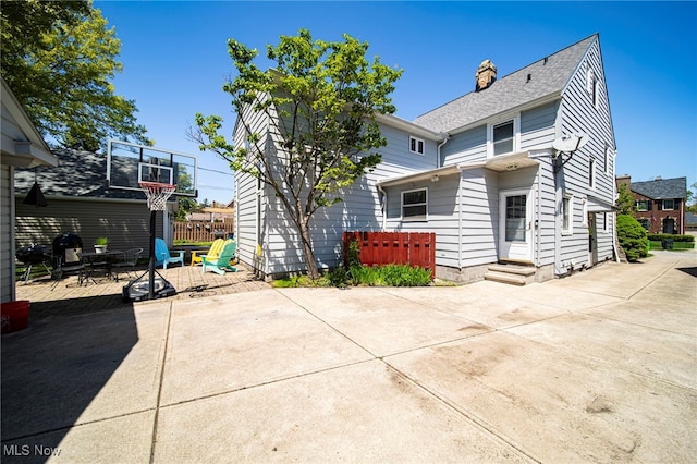 rear view of house featuring a patio, entry steps, a chimney, and a shingled roof