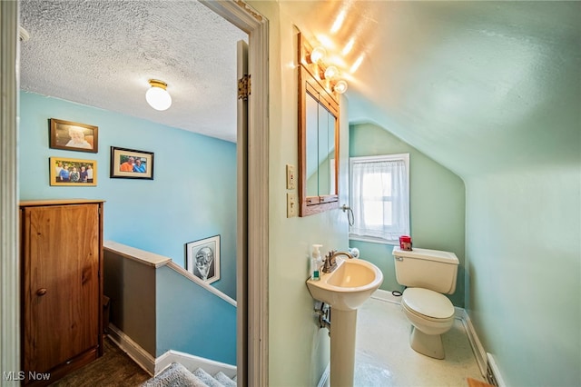 half bath featuring toilet, vaulted ceiling, baseboards, a sink, and a textured ceiling