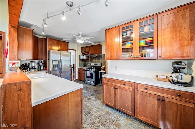 kitchen featuring appliances with stainless steel finishes, a sink, brown cabinetry, decorative backsplash, and light countertops