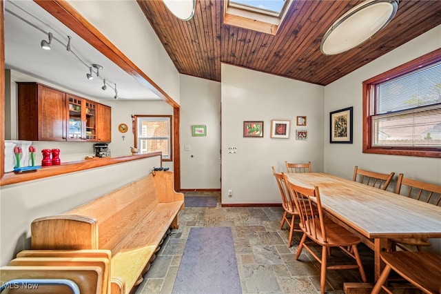 dining space featuring stone tile floors, baseboards, wood ceiling, and a skylight
