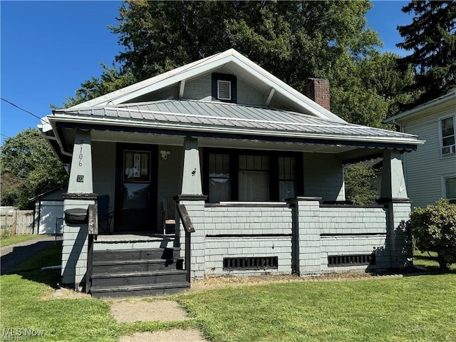 bungalow featuring covered porch, a chimney, a front yard, and metal roof