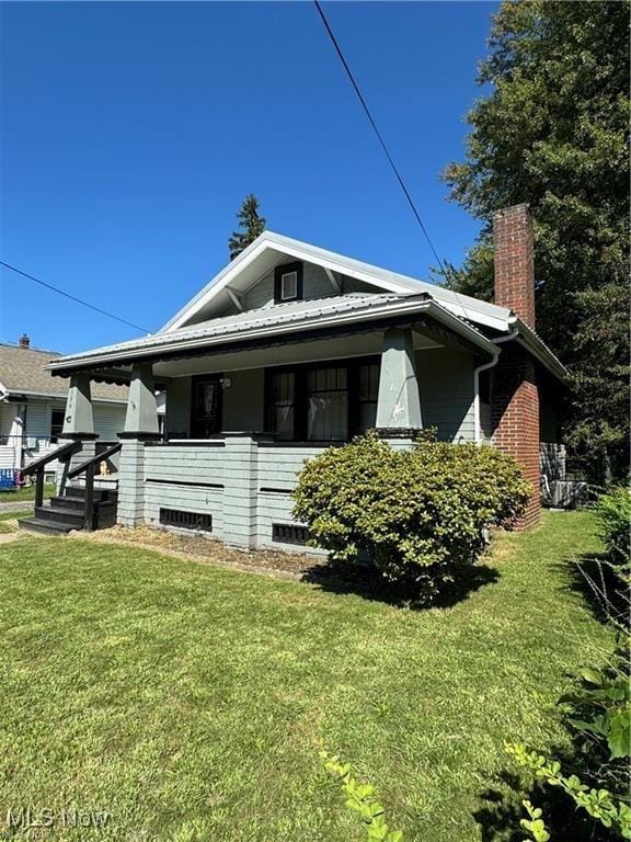 view of side of home with a lawn, a chimney, and a porch