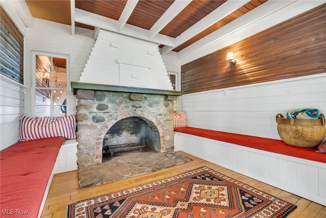 living area featuring hardwood / wood-style flooring, beamed ceiling, a fireplace, wooden walls, and wood ceiling