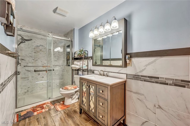 full bath with tile walls, a shower stall, toilet, vanity, and wood finished floors