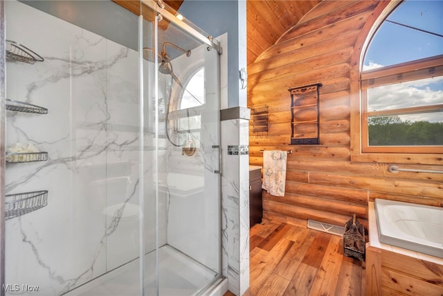 full bathroom with rustic walls, wood-type flooring, vanity, a marble finish shower, and vaulted ceiling