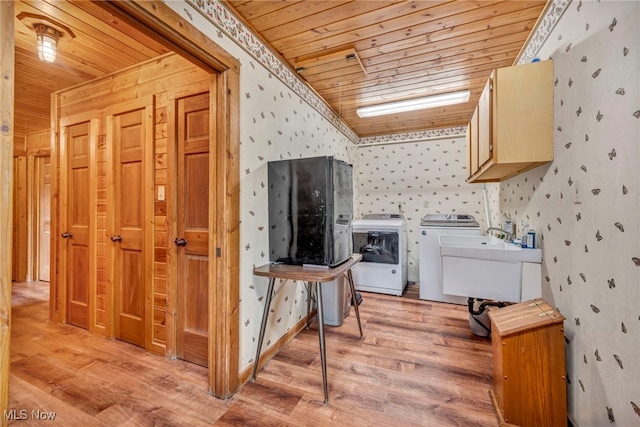 clothes washing area featuring wood ceiling, wallpapered walls, cabinet space, washer and dryer, and light wood-type flooring