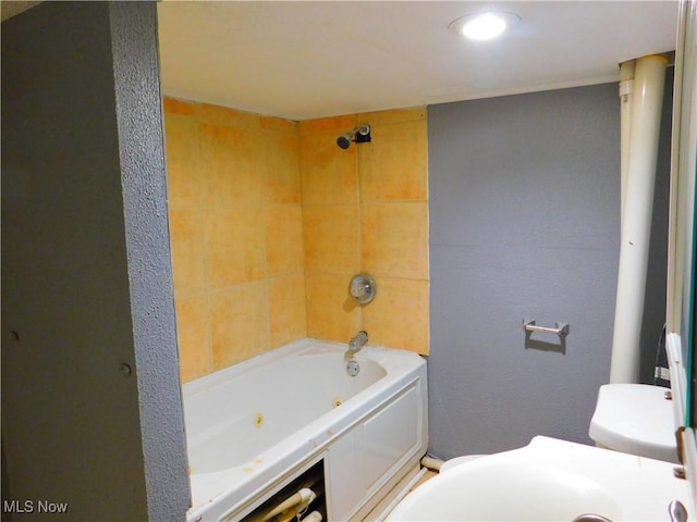 bathroom featuring a textured wall, a combined bath / shower with jetted tub, and toilet