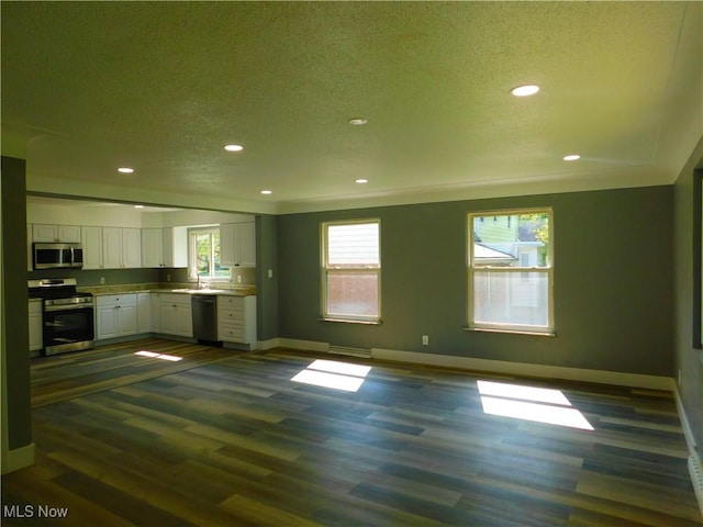 kitchen with appliances with stainless steel finishes, baseboards, plenty of natural light, white cabinets, and a textured ceiling