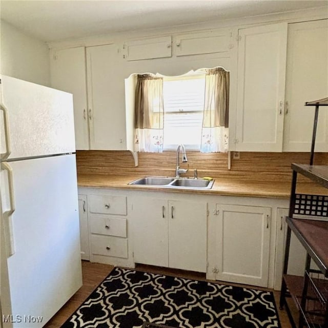 kitchen with freestanding refrigerator, a sink, white cabinets, and light countertops