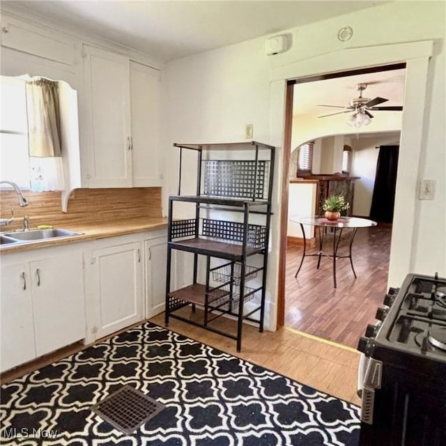 kitchen with a sink, white cabinetry, wood finished floors, gas stove, and arched walkways