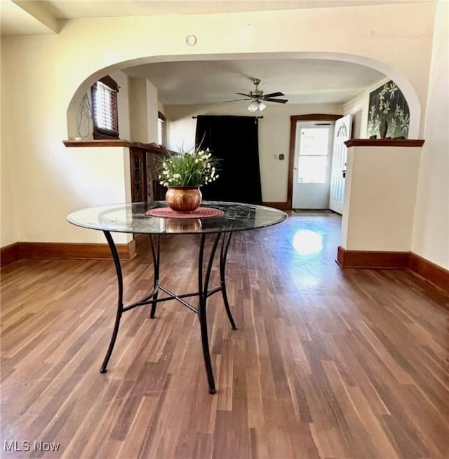 dining area with wood finished floors, baseboards, a ceiling fan, and arched walkways