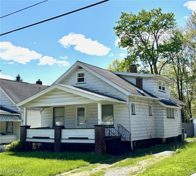 bungalow with covered porch, a chimney, a front lawn, and roof with shingles