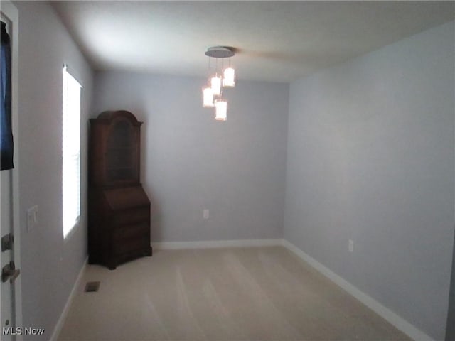 empty room featuring a chandelier, light carpet, and baseboards