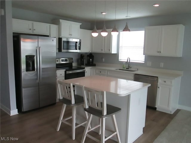 kitchen featuring stainless steel appliances, a sink, dark wood-style floors, white cabinetry, and a center island