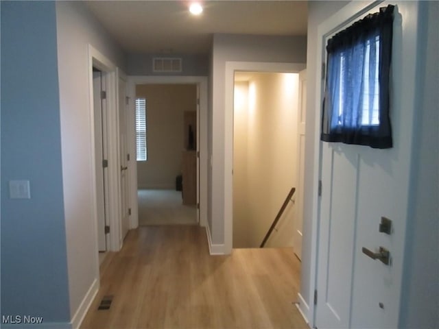 hall with an upstairs landing, light wood-type flooring, and baseboards