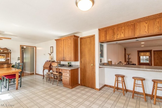 7101 Reynolds Rd, Mentor, OH 44060 - kitchen featuring brown cabinets, light countertops, baseboards, a kitchen breakfast bar, and ceiling fan