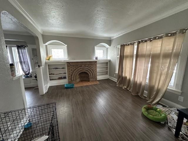 unfurnished living room with arched walkways, crown molding, wood finished floors, a textured ceiling, and baseboards