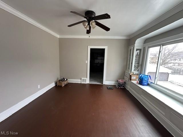 empty room featuring baseboards, a ceiling fan, crown molding, and wood finished floors